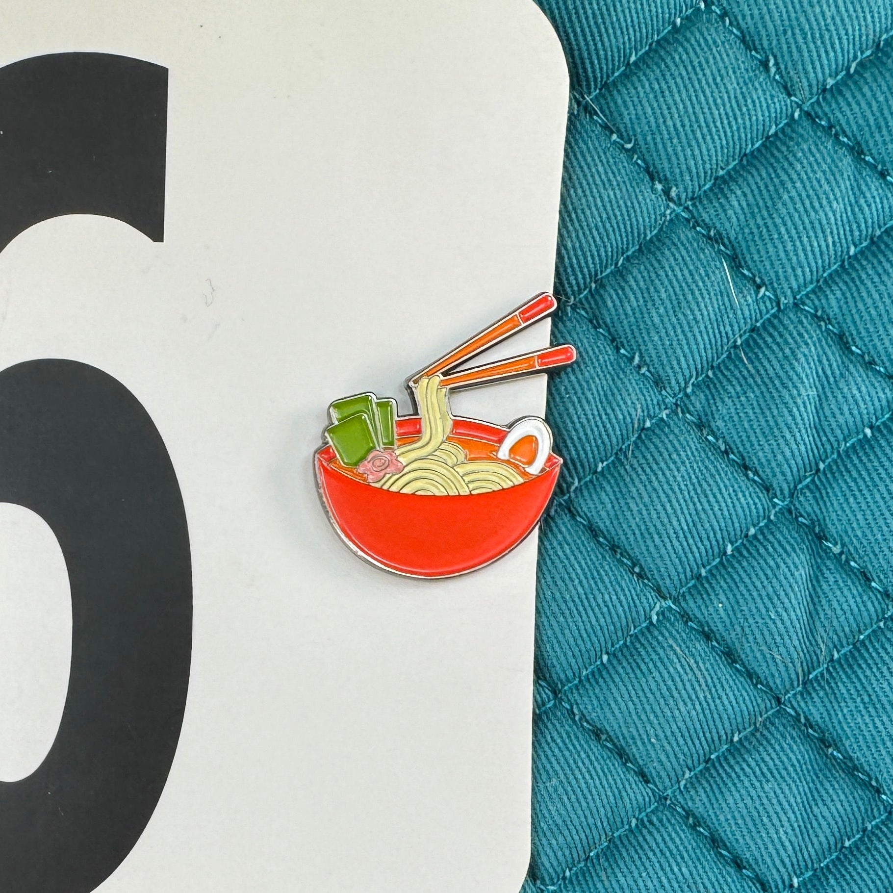Teal quilted surface with a number 96 label and a small icon of noodles.