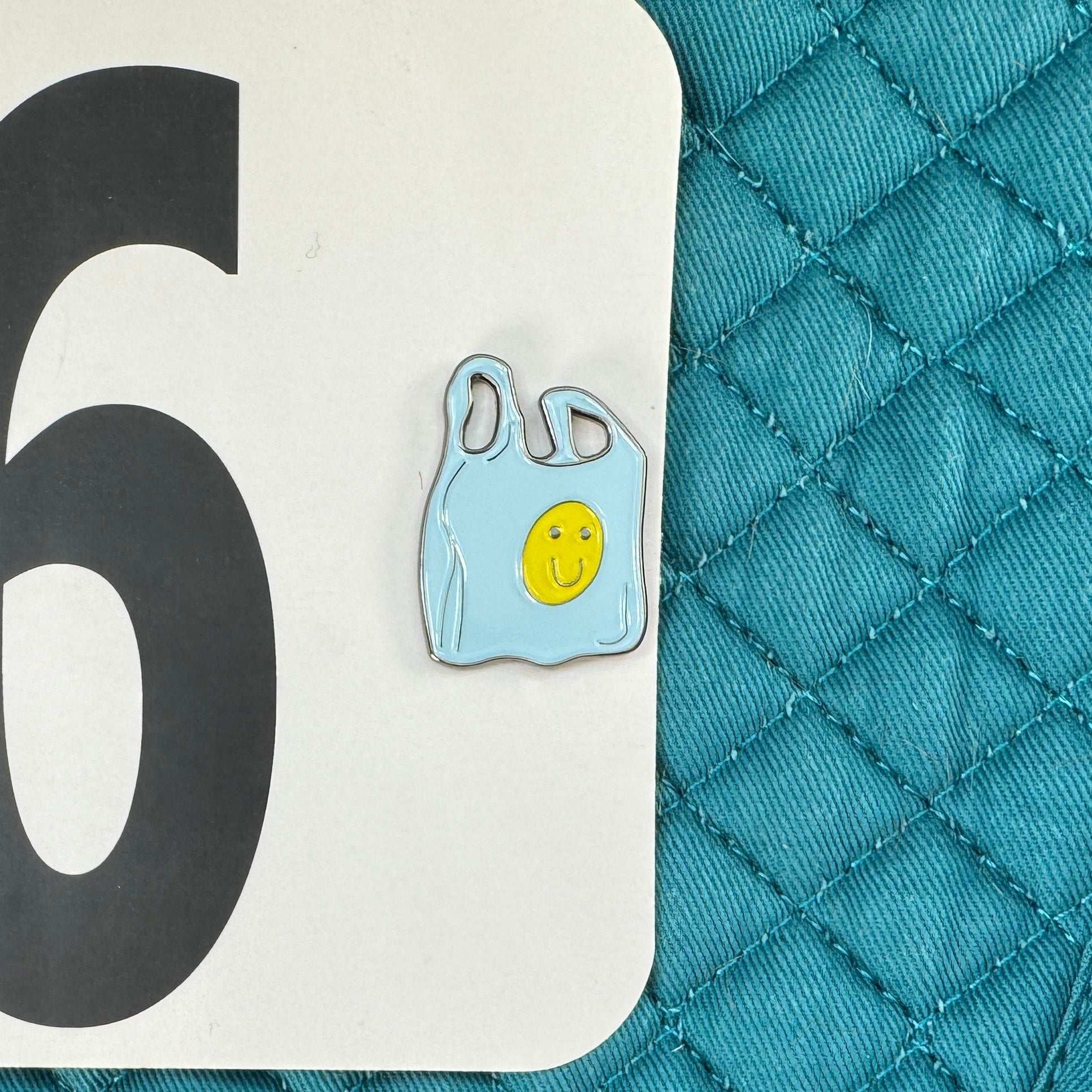 Teal quilted mat with number 96 and plastic bag pin on a black background