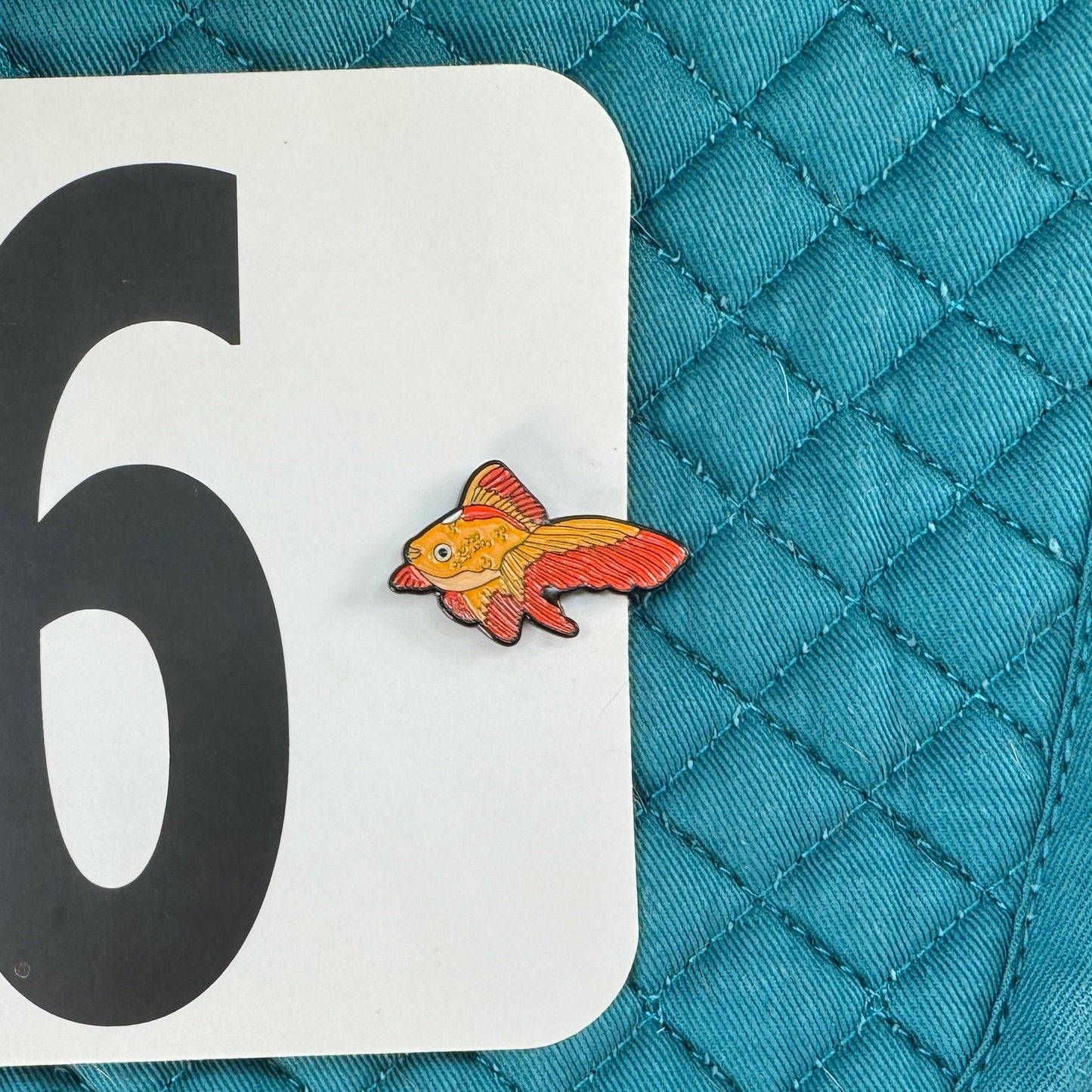 Teal quilted saddle pad with number 96 and goldfish sticker on a black background